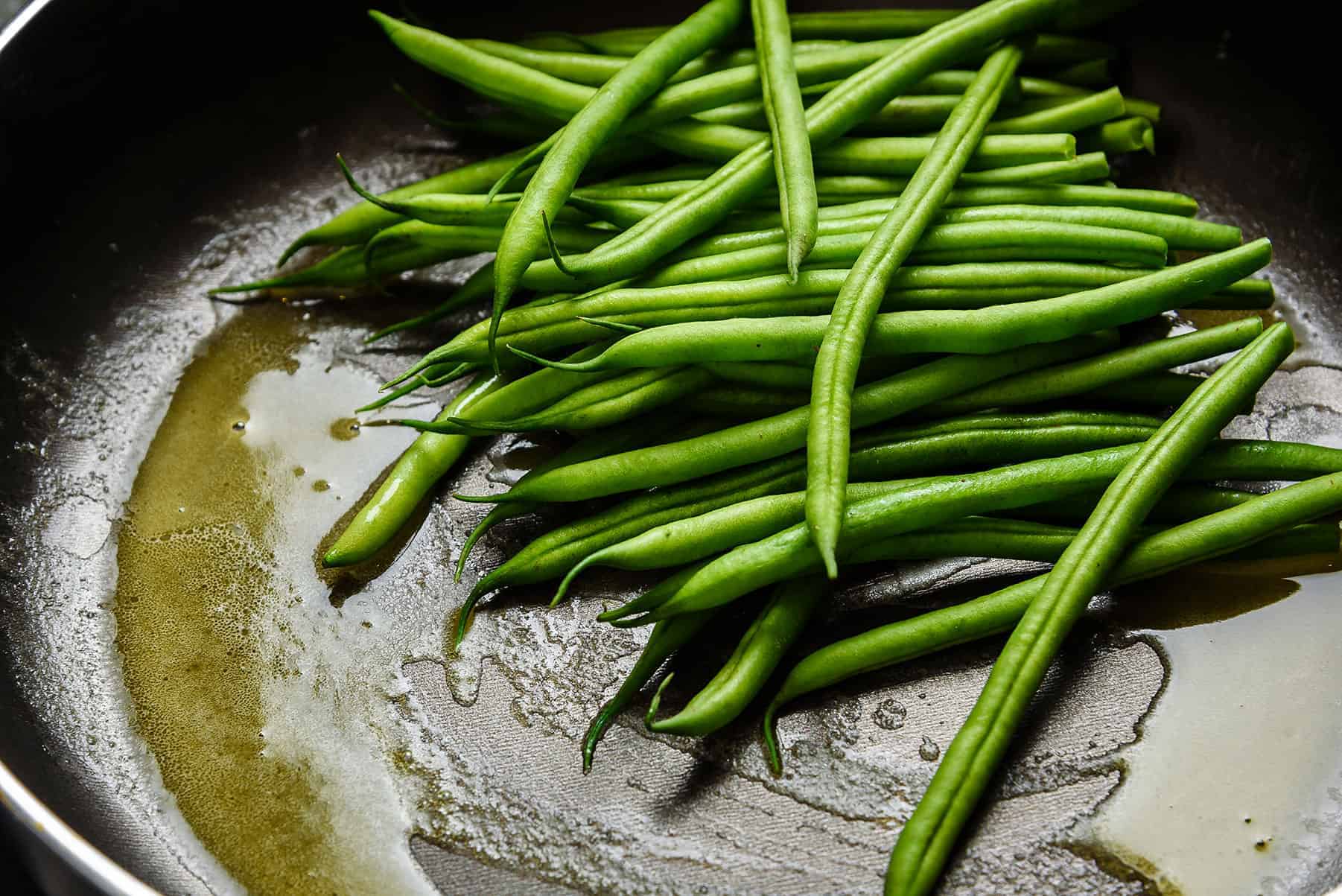Adding green beans to melted butter in a frying pan