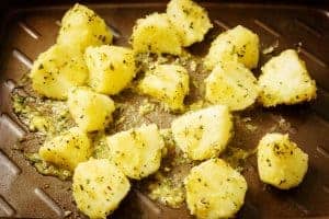 Potatoes covered with butter mixture on a roasting tray