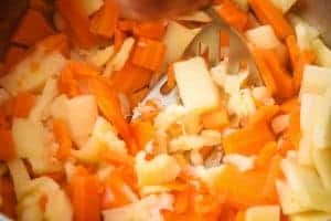 Lightly mashing the cooked carrots and parsnips with a hand-held potato masher