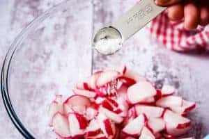 Sprinkling the salt over sliced radish in a bowl